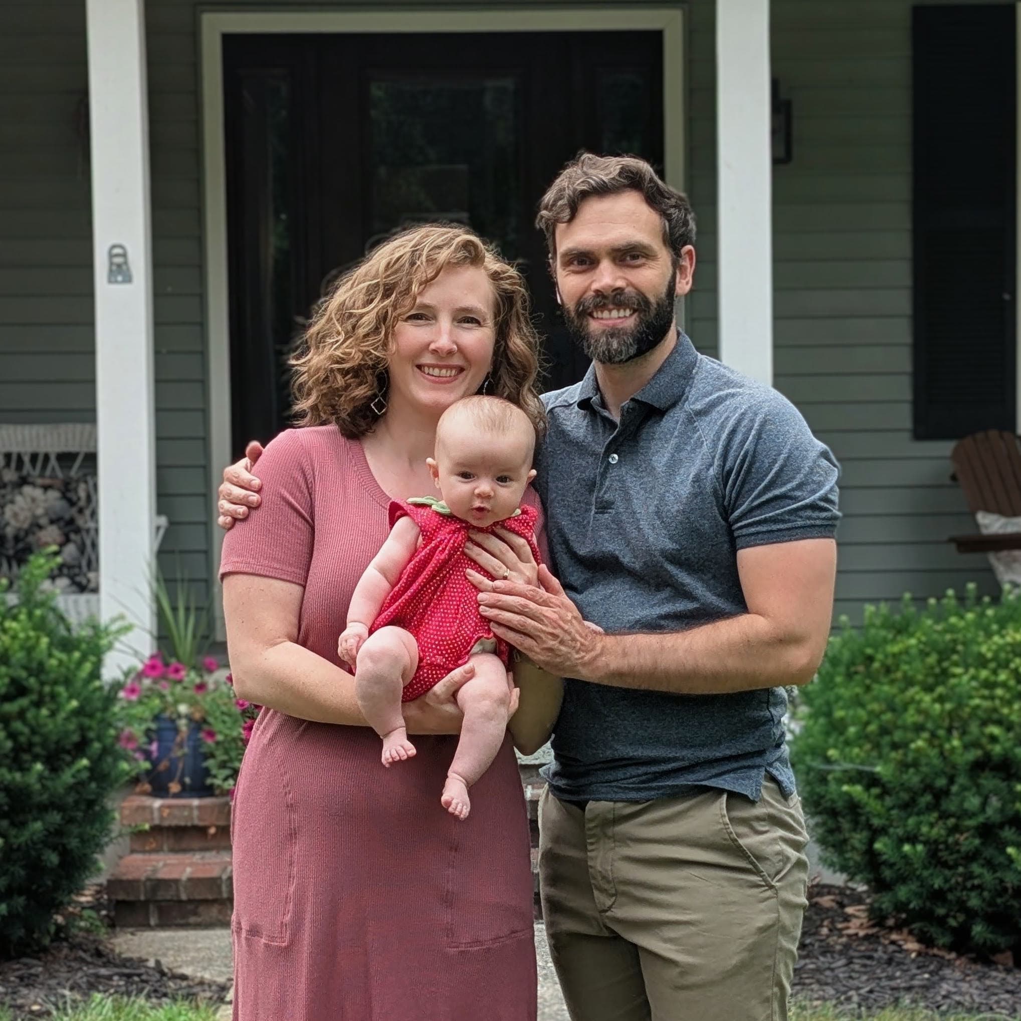 Liz and Kyle holding their daughter in front of their home