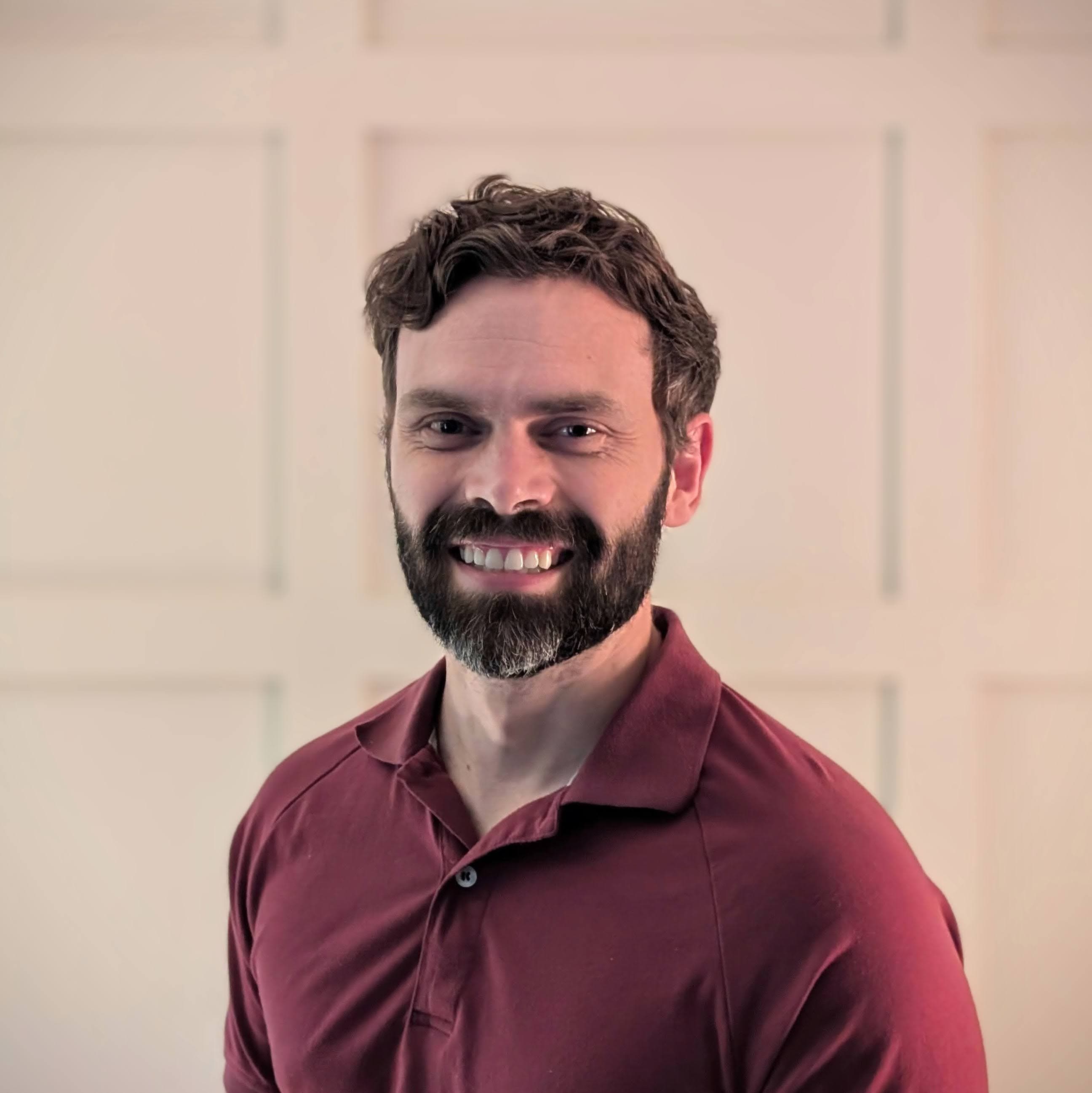 Kyle, smiling in a portrait against a paneled wall